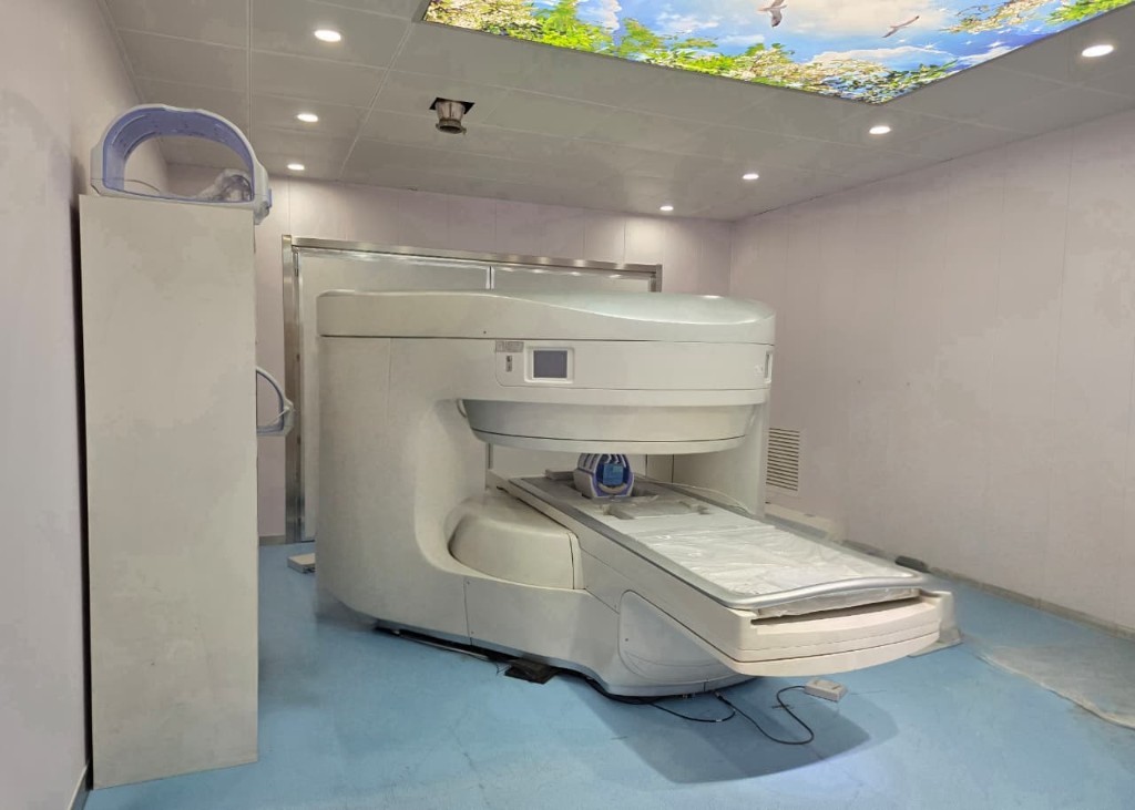 Open permanent-magnet MRI in Kenya — C-shaped scanner with patient table, calming sky-ceiling lighting, and modern clinical room.